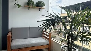 Un balcón con un banco de madera, un sofá gris y plantas en macetas.