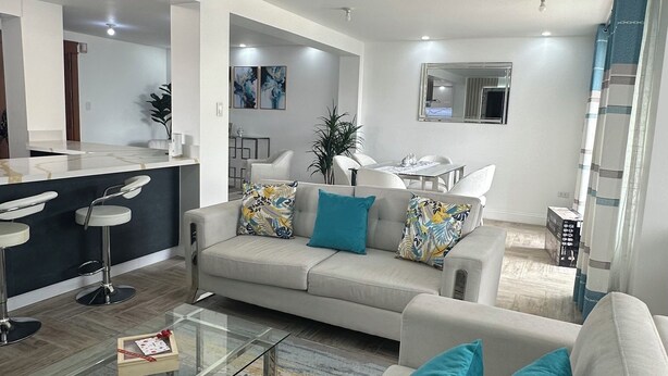 Una sala moderna con un sofá, una mesa de centro y un área de comedor al fondo.