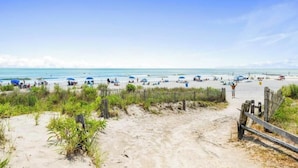 Une plage avec un sentier de sable menant à l’eau, des parasols et des gens qui profitent de la plage.