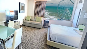 Une chambre d’hôtel avec un lit, un canapé, un bureau avec une télévision et une grande fenêtre donnant sur l’océan et une grande roue.