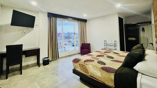 A hotel room with a bed, a desk, a chair, a TV, and a view of the city through the window. - HOTEL ESTRELLA ZACATLAN (Zacatlán)