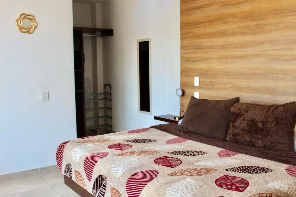 Un dormitorio con cama, cabecero de madera, mesita de noche y lámpara de pared.