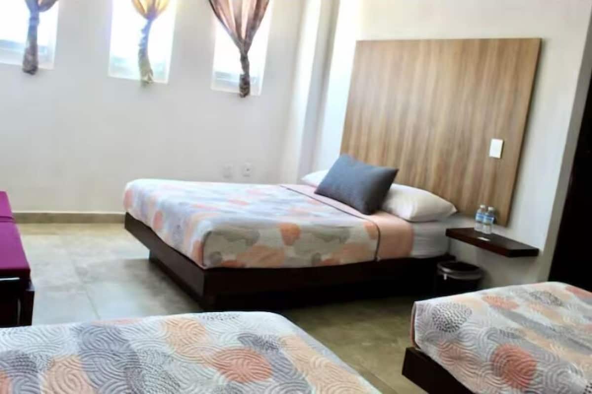 Habitación de hotel con cama, dos mesitas de noche, cortinas y vistas al exterior.