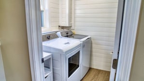 Une buanderie équipée de deux machines à laver et d’un sèche-linge, avec un plancher en bois et une fenêtre.