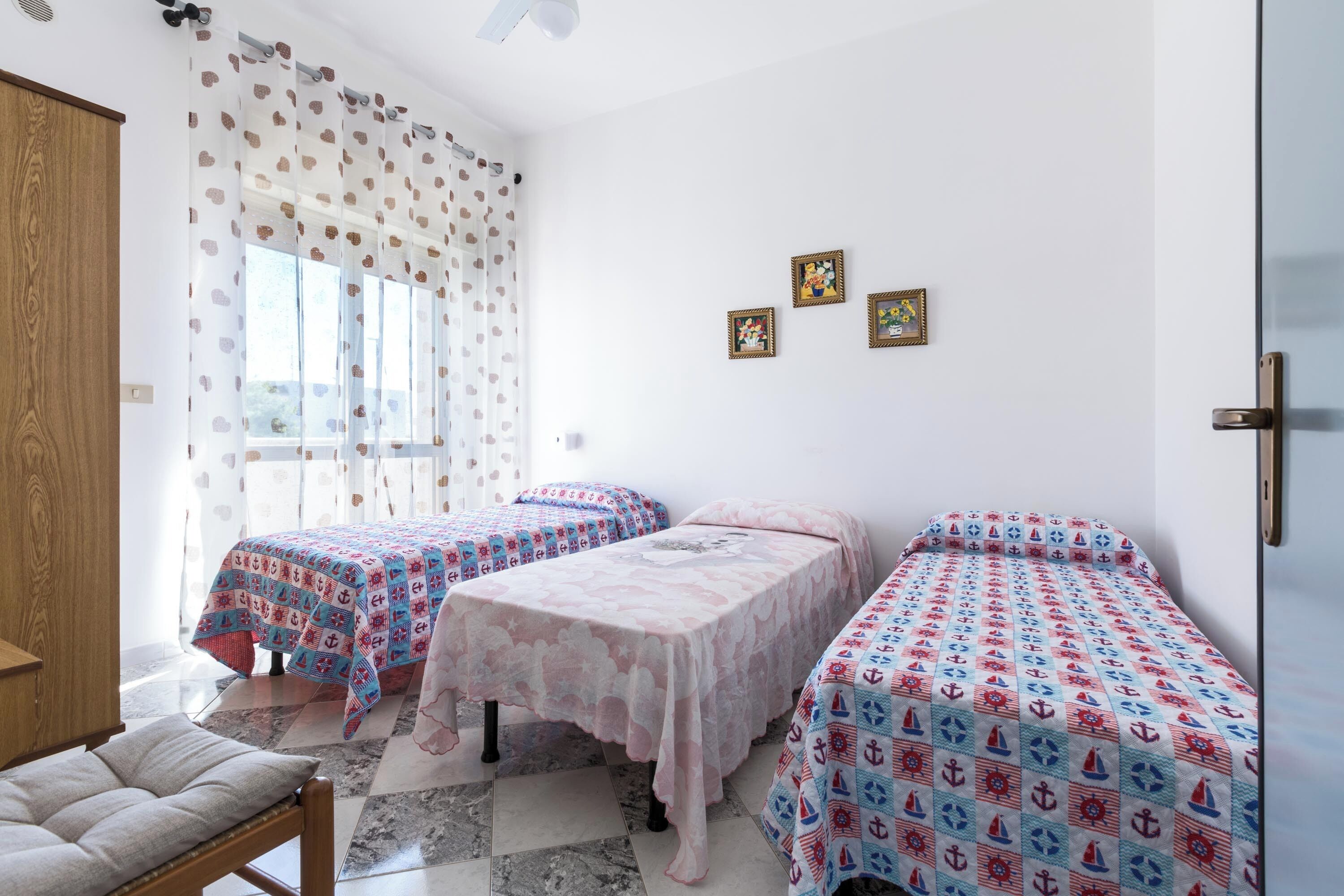 A room with two beds, a wooden wardrobe, and a window with patterned curtains.