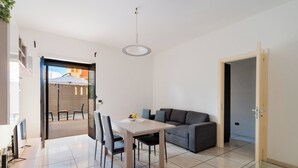 Een moderne woonkamer met een eethoek, een grijze bank en een televisie op een dressoir.