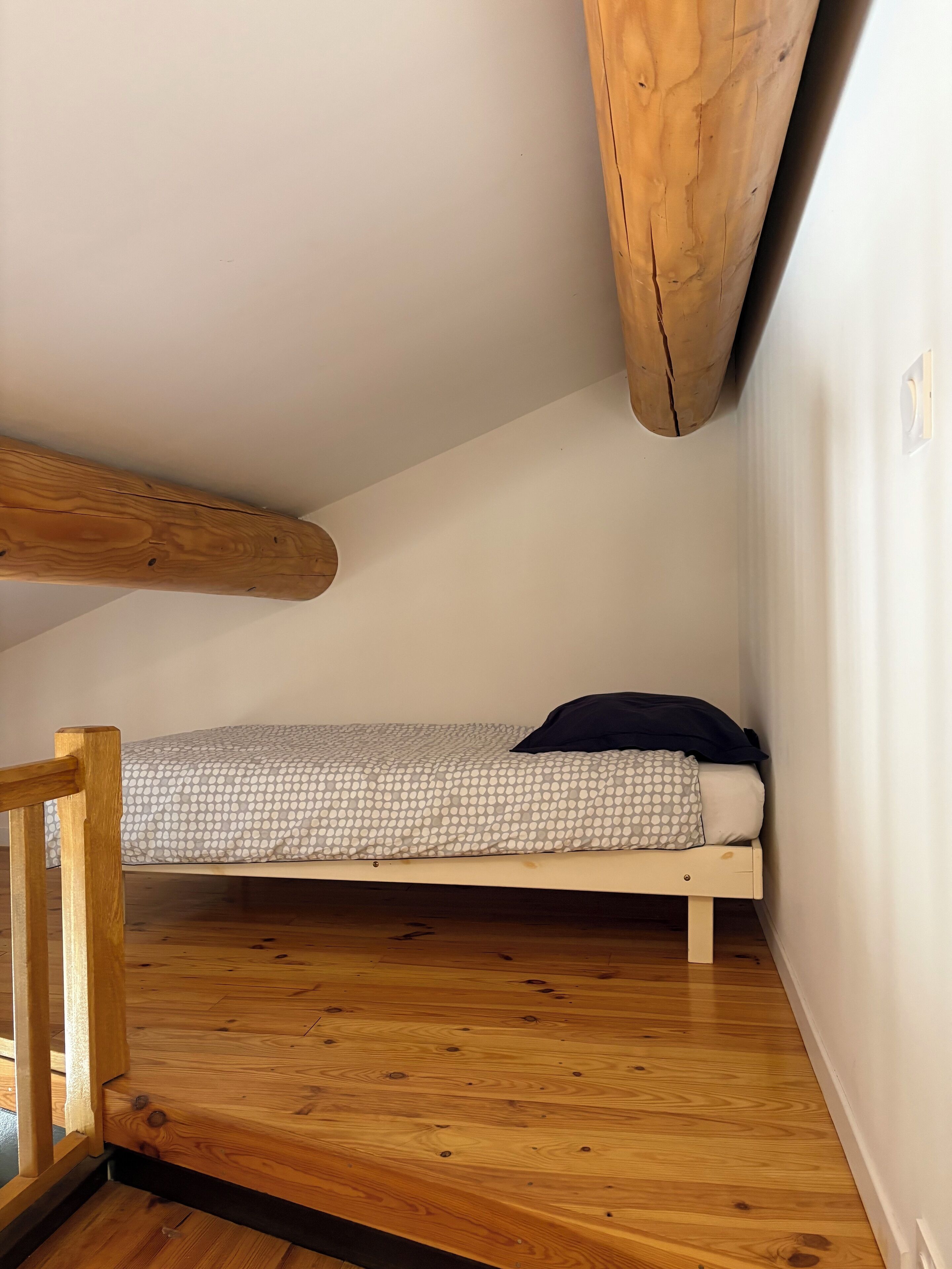 Una habitación pequeña con cama individual, piso de madera y techo inclinado.