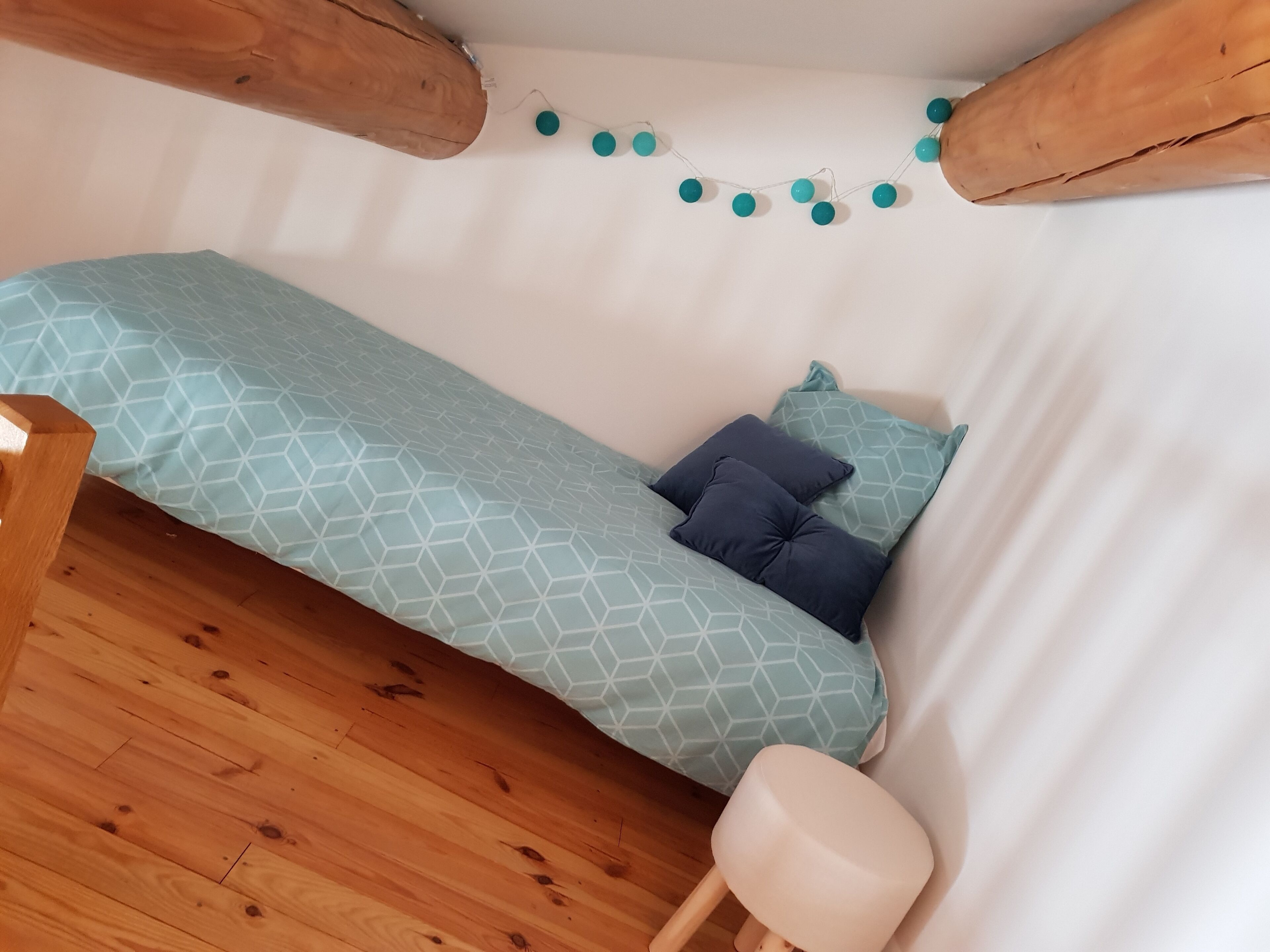 Une petite pièce chaleureuse, avec un lit simple, un plancher en bois et une guirlande de petites lumières turquoise accrochée au mur.