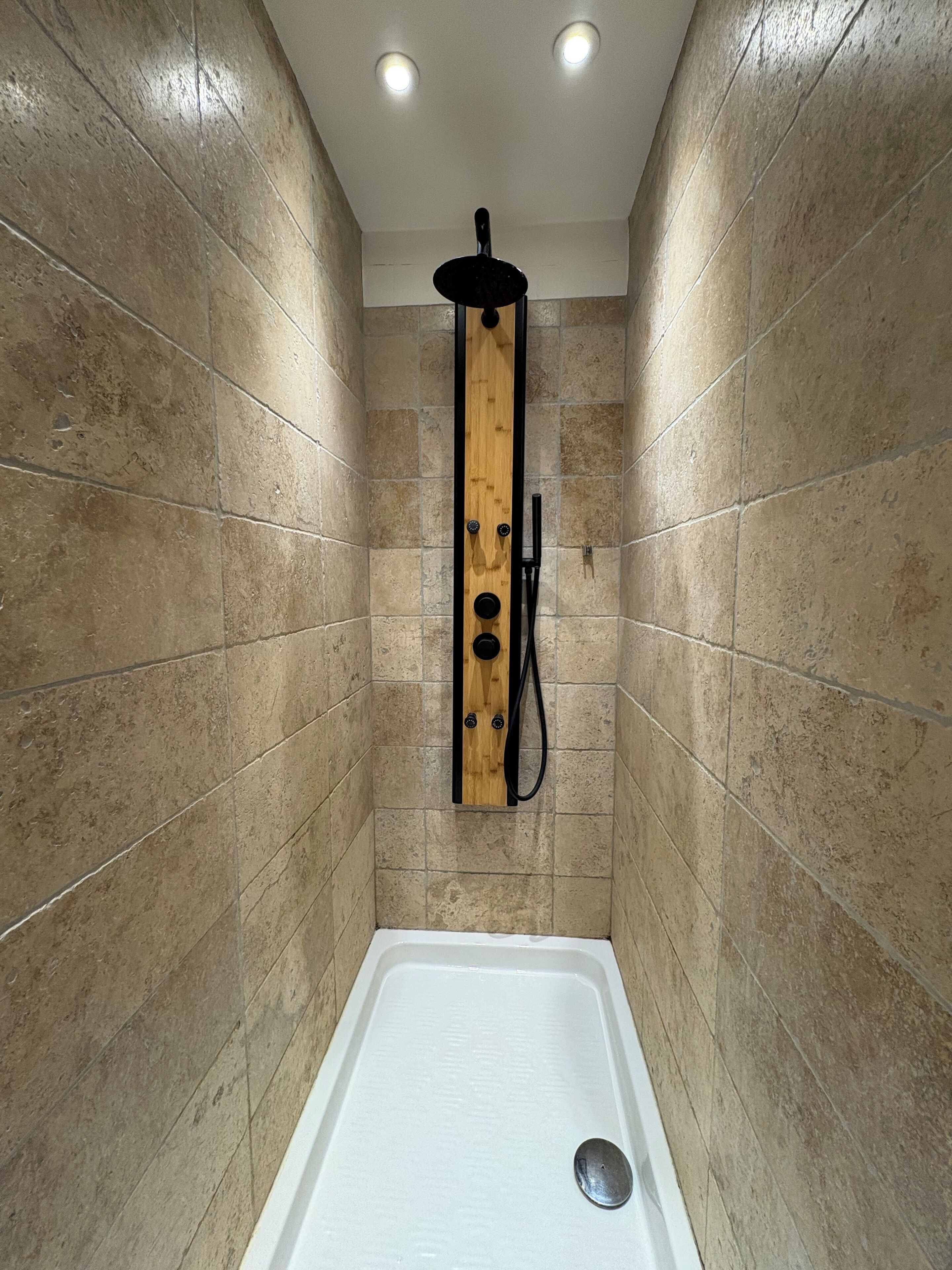 Un box de ducha con panel de madera, paredes con azulejos color beige y una bañera blanca.