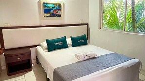 A hotel room with a bed, a nightstand, a painting, an air conditioner, and a window with a view of palm trees. - Hotel Mar Azul Neiva (Neiva)