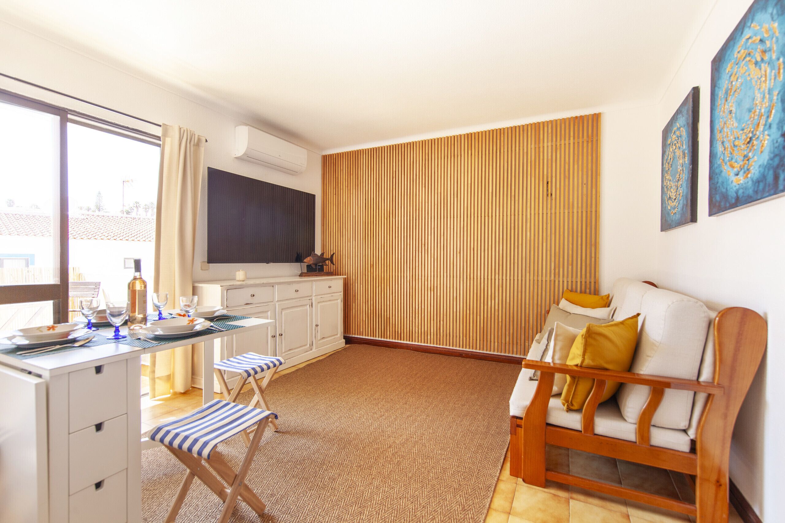 A compact living space with a kitchenette, a dining area with a table and chairs, a sofa, and a large window.
