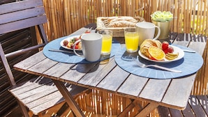 A wooden table with a basket of pastries, two plates with fruit, a pitcher, and glasses of orange juice.