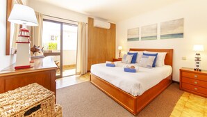 Une chambre d’hôtel avec un grand lit, une table de chevet en bois, un bureau avec une lampe, un fauteuil en osier et une vue sur l’extérieur grâce à une porte coulissante.