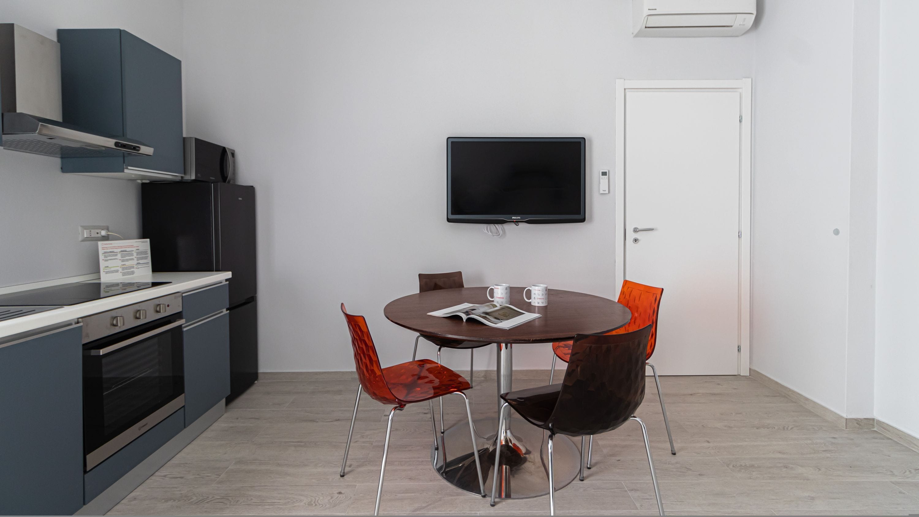 Una cucina moderna con zona pranzo, inclusi televisore a parete, frigorifero e piano cottura.