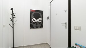 A hallway with a coat rack, a door with a light switch, and a poster on the wall. - Italianway Comfort - Copernico 47 B (Milan)