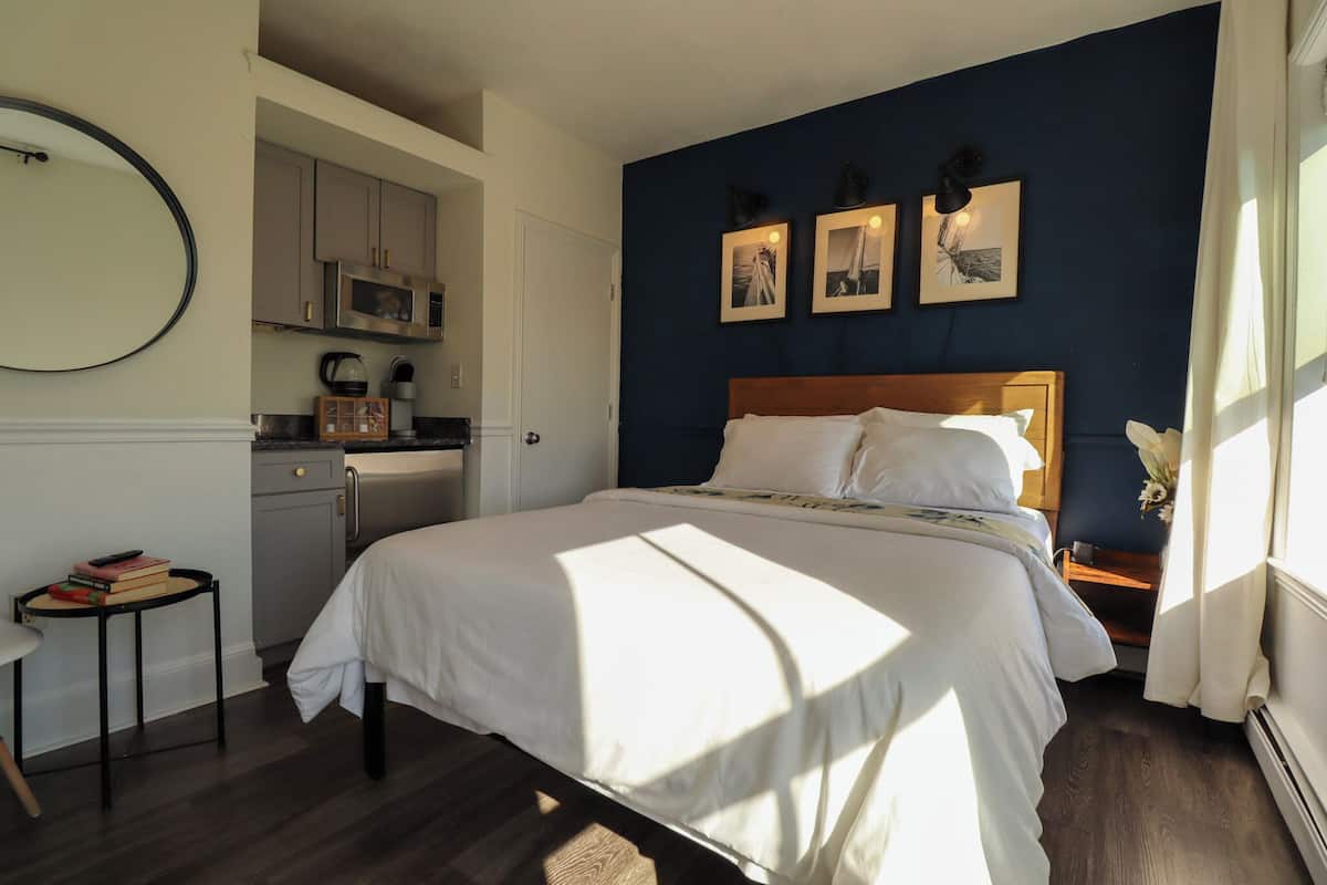 Una camera da letto con un letto, una scrivania, un angolo cottura e una parete blu scuro con quadri.