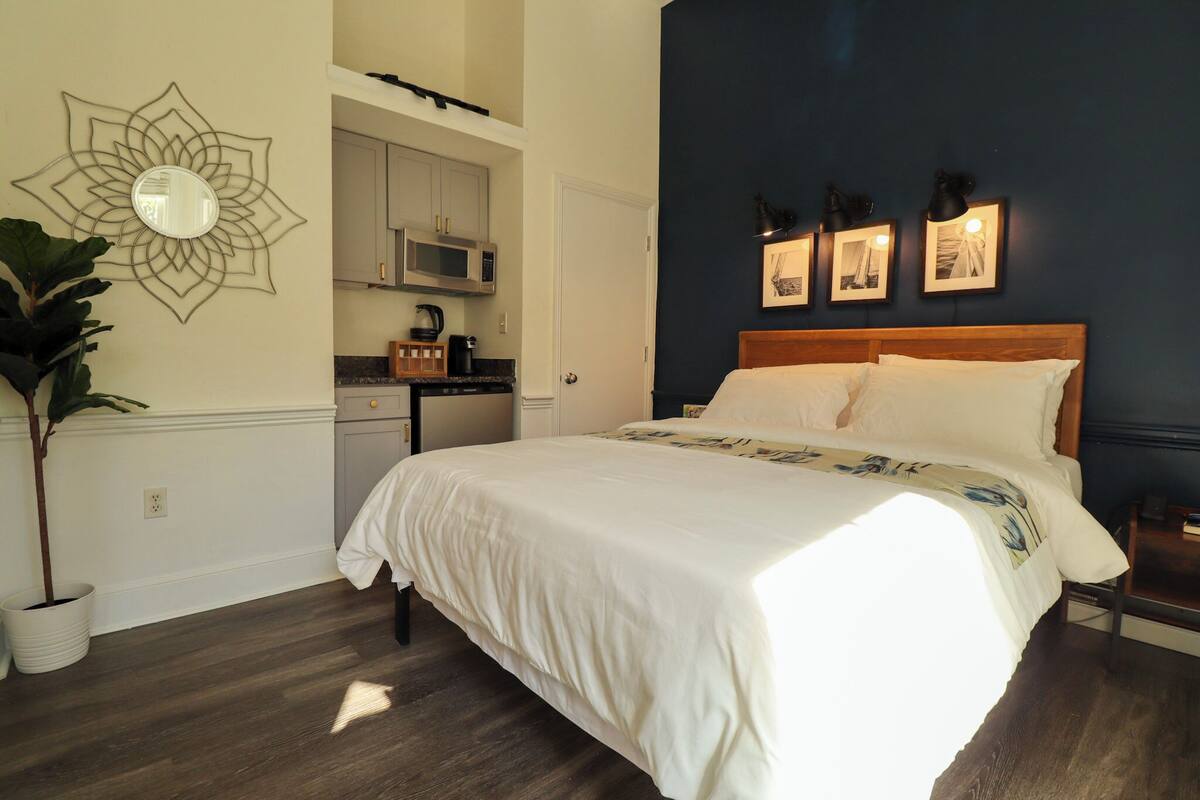Una camera da letto con un letto, uno specchio fissato alla parete, un forno a microonde e quadri appesi al muro.