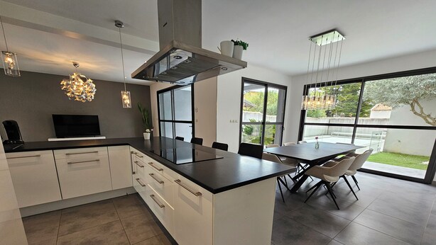 A modern kitchen with white cabinetry, a black countertop, and a dining area with a table and chairs.