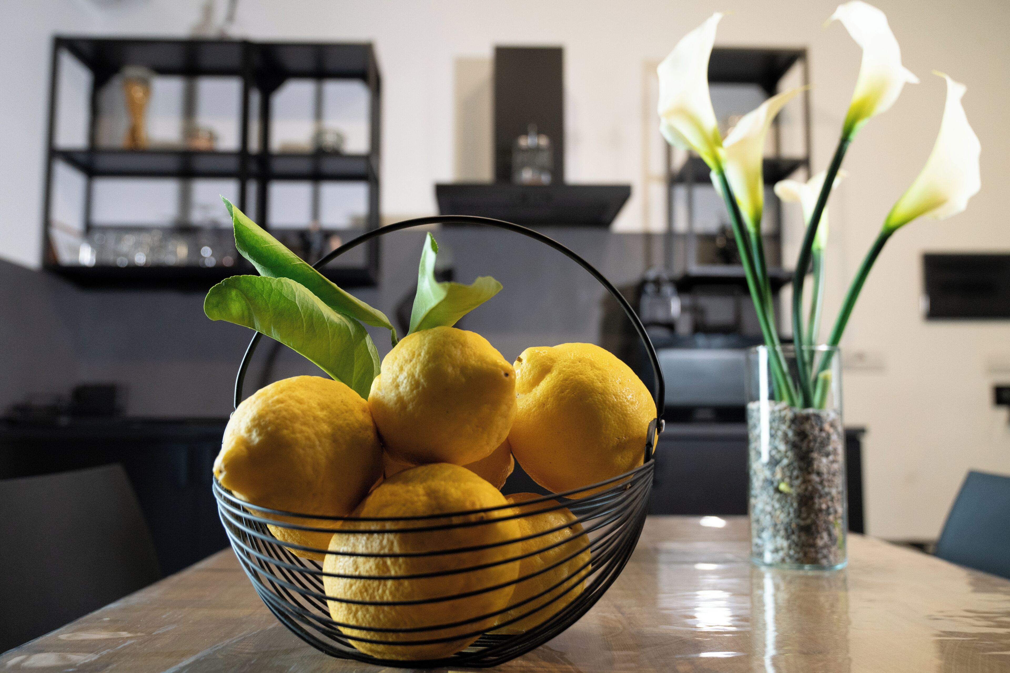Un bol de citrons sur une table, avec un vase de fleurs en arrière-plan.