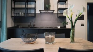 Une cuisine moderne avec des meubles de couleur sombre, un îlot central et une table à manger agrémentée d’un vase de fleurs et d’une bougie.