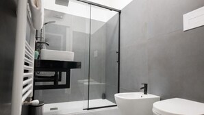 Un bagno moderno con cabina doccia in vetro, un lavandino bianco e due servizi igienici.