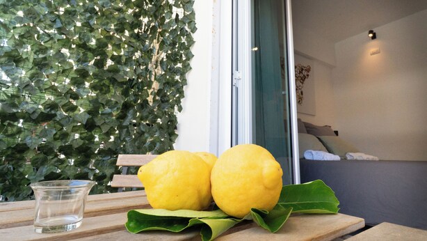 Un tavolo con limoni e un bicchiere, una panca di legno e un muro ricoperto di foglie verdi.