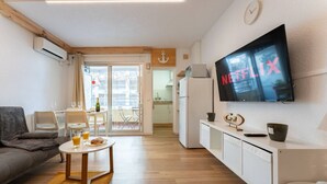 Un salon moderne doté d’un téléviseur à écran plat, d’un canapé, d’un coin repas avec une table et des chaises, et d’un coin cuisine avec un réfrigérateur et un four à micro-ondes.