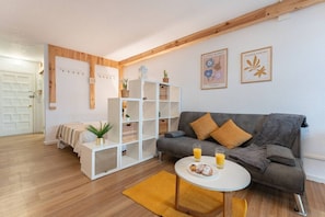 A living room with a grey sofa, a white coffee table with drinks, a bookshelf, and a door in the background.