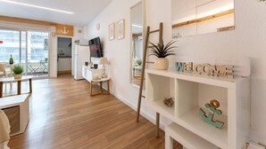 Un salon moderne avec un plancher en bois, un téléviseur, une plante et une étagère ornée d’objets décoratifs.