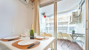 Un coin repas avec une table dressée pour deux personnes, une bouteille de vin et une vue sur la ville grâce à de grandes fenêtres.