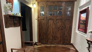 Ein Holzboden mit Teppich in der Mitte, eine hölzerne Bank und eine große Holztür mit Glasfeldern.