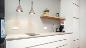 A modern kitchen with white cabinetry, a countertop, a sink, a coffee maker, and pendant lights. - Comfy Central Apartment (Reykjavík)