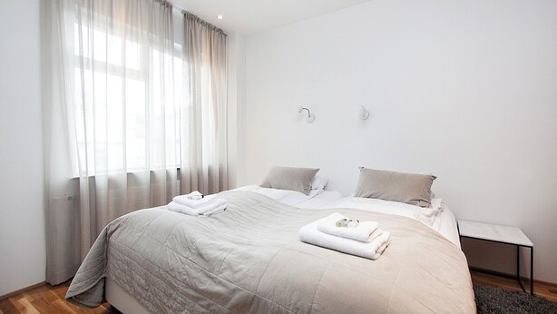 A modern bedroom with a large bed, two bedside tables, and a window with sheer curtains. - Comfy Central Apartment (Reykjavík)