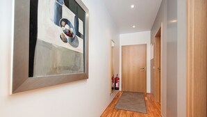 A hallway with wooden flooring, a large abstract painting on the left wall, and a door at the end. - Comfy Central Apartment (Reykjavík)