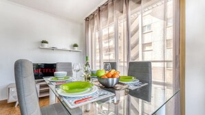 A modern dining area with a glass table, grey upholstered chairs, a bowl of fruit, and a television displaying Netflix. - Bambu Salou / Tropical / Chill out / Pool / Wifi (Salou)