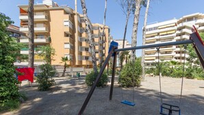 A playground with swings and a climbing structure, surrounded by apartment buildings. - Bambu Salou / Tropical / Chill out / Pool / Wifi (Salou)