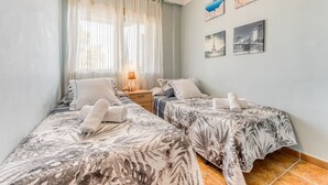 A bedroom with two beds, a nightstand, a lamp, and a window with sheer curtains. - Bambu Salou / Tropical / Chill out / Pool / Wifi (Salou)