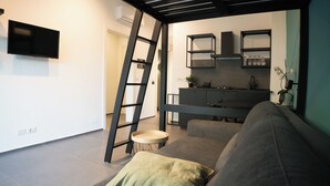 A modern living room with a grey sofa, a small round table, and a ladder against the wall. - Oktò apartments Milazzo: Studio apartment (Milazzo)