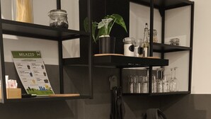 A modern kitchen with black cabinetry, a gas stove, a sink, and a shelf with kitchen utensils and a potted plant. - Oktò apartments Milazzo: Studio apartment (Milazzo)
