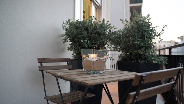 A wooden table with a glass candle holder on it, placed on a balcony with potted plants in the background. - Oktò apartments Milazzo: Studio apartment (Milazzo)