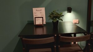 A dining table with a menu stand, two chairs, a potted plant, and a wall-mounted light fixture. - Oktò apartments Milazzo: Studio apartment (Milazzo)