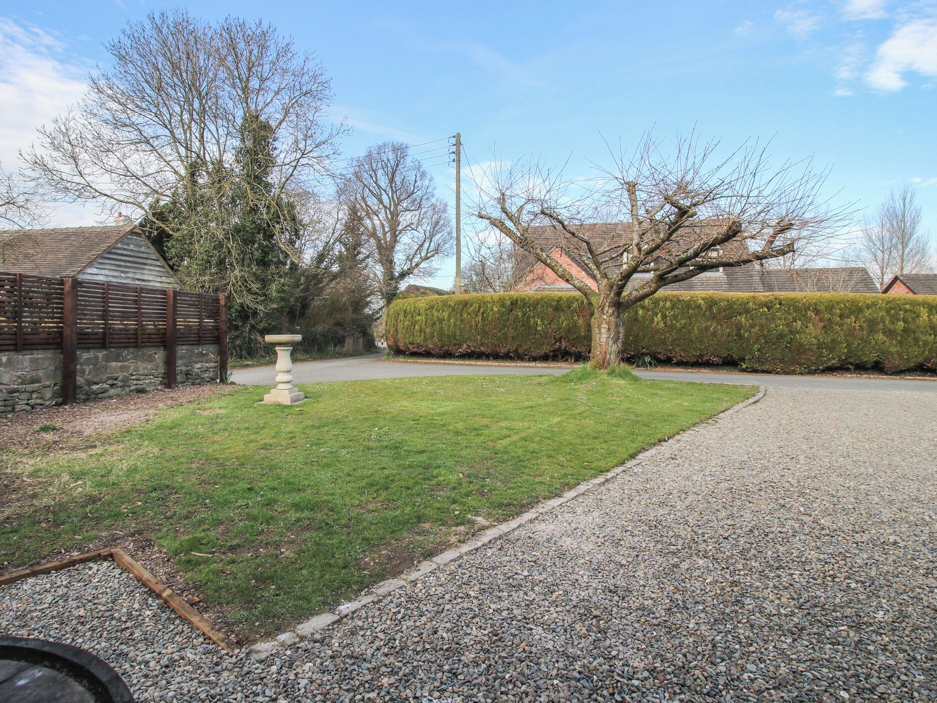A gravel driveway leading to a house with a stone wall and a wooden fence.