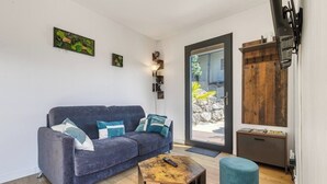 Una sala moderna con un sofá azul oscuro, una mesa de centro de madera y un reposapiés azul. Hay un mueble de madera con ganchos en la pared, y una pequeña estantería con adornos.