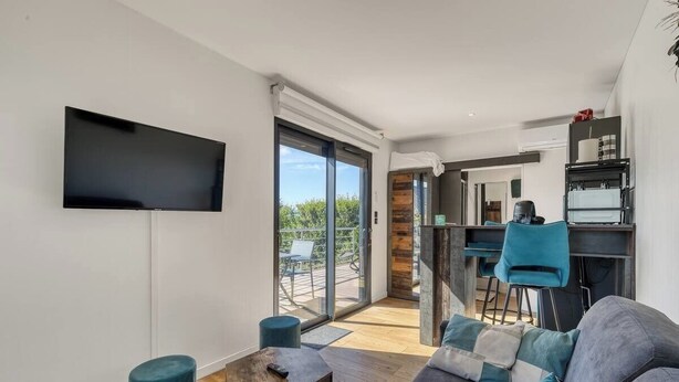 Una sala de estar moderna con un sofá gris, un televisor de pantalla plana montado en la pared y un puerta corredera de vidrio que da a un balcón.