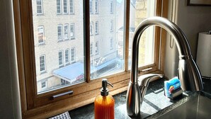 A kitchen with a window view of a building with a tower, a stainless steel faucet, and a soap dispenser. - Brick Haven, 2 bedroom condo in the Grand Traverse Commons (Traverse City)