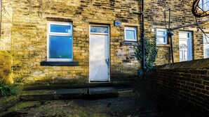 Un bâtiment en briques doté de deux portes et de fenêtres, d’un petit espace jardin et d’un mur en briques.