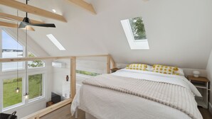 Un dormitorio con cama, ventana, tragaluz y vistas a la vegetación.