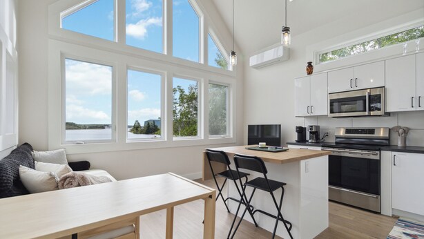 Una cocina moderna con armarios blancos, electrodomésticos de acero inoxidable y un amplio ventanal con vista a un lago.