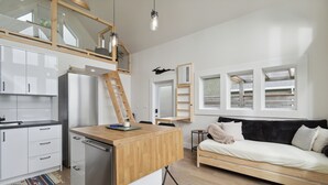 Una cocina moderna con una isla de madera, un refrigerador empotrado y un dormitorio entre pisos con un sofá negro.
