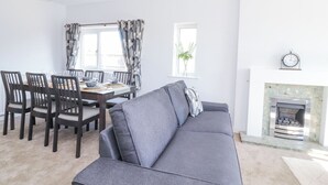 A modern living room with a grey sofa, dining table with chairs, a fireplace, and a window with curtains. - 38 Clive Avenue (Lytham St. Anne's)